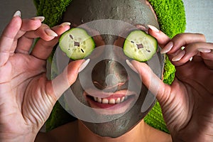 Beautiful young woman with facial mask on her face holding slices of cucumber