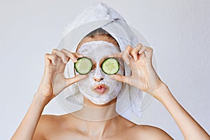 Beautiful young woman with facial mask on her face holding slices of cucumber. Skin care and treatment, spa, natural beauty and