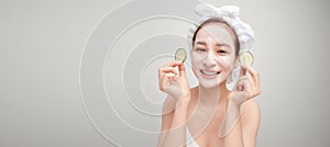 Beautiful young woman with facial mask on her face holding slices of fresh cucumber