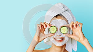 Beautiful young woman with facial mask on her face holding slices of cucumber. Skin care and treatment, spa, natural beauty and