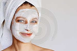 Beautiful young woman with facial mask on her face. Skin care and treatment, spa, natural beauty and cosmetology concept