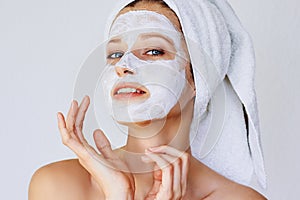 Beautiful young woman with facial mask on her face. Skin care and treatment, spa, natural beauty and cosmetology concept