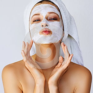 Beautiful young woman with facial mask on her face. Skin care and treatment, spa, natural beauty and cosmetology concept