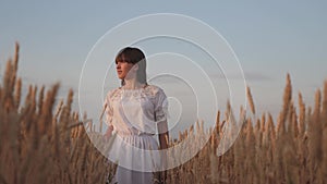 Beautiful young woman farmer enjoying nature in a wheat field, sunset. a free girl walks across the field, touching her