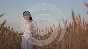 Beautiful young woman farmer enjoying nature in a wheat field, sunset. a free girl walks across the field, touching her