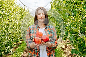 Beautiful young woman farmer hold red ripe apple in hands calm facial expression.