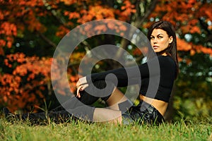 Beautiful young woman in fashionable black clothes sitting in the park.