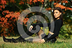 Beautiful young woman in fashionable black clothes sitting in the park