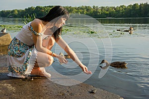 Beautiful young woman is feeding birds on the lake. Beautiful yo