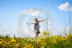 Beautiful young woman on a field with green grass and yellow dandelion flowers in a sunny day. Girl on nature with yellow flowers