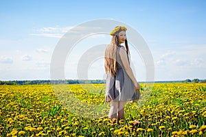 Beautiful young woman on a field with green grass and yellow dandelion flowers in a sunny day. Girl on nature with yellow flowers