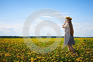 Beautiful young woman on a field with green grass and yellow dandelion flowers in a sunny day. Girl on nature with yellow flowers