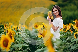 Beautiful young Woman in the field of sunflowers. girl with long brunette hair with sunflower in hand. Summer time