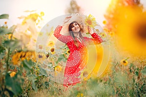 Beautiful young woman in field sunflowers in red dress and hat, sunlight
