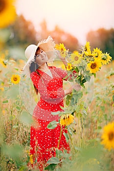 Beautiful young woman in field sunflowers in red dress and hat, sunlight