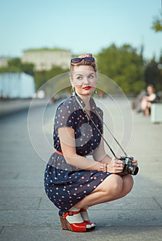 Beautiful young woman in fifties style holding retro camera