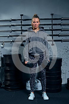 Beautiful young woman fitness instructor wearing a sports suit doing an exercise lunges with dumbbells on a gray