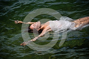 Beautiful young woman floating in ocean or sea water, relaxing and taking care of herself. Fashion portrait of graceful
