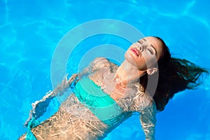 Beautiful young woman floating in pool and relaxing
