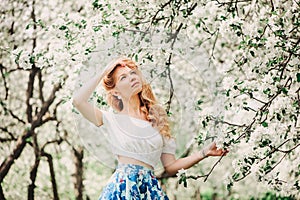 Beautiful young woman in floral maxi skirt walking in blooming spring garden