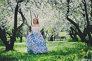 Beautiful young woman in floral maxi skirt walking in spring