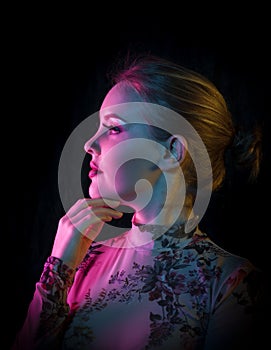 Beautiful young woman with floral patterned shirt posing in creative pink, blue and orange light in front of a black background