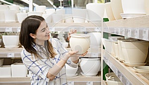 A beautiful young woman in a flower shop chooses a pot for flowers