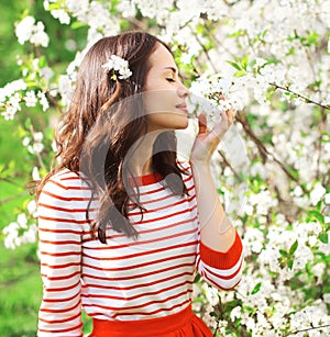 Beautiful young woman in a flowering spring garden enjoying petals of flowers
