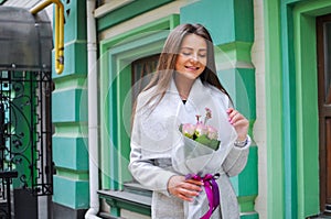 Beautiful young woman with flowers bouquet at city street. Spring portrait of pretty female