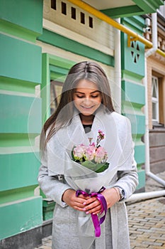 Beautiful young woman with flowers bouquet at city street. Spring portrait of pretty female