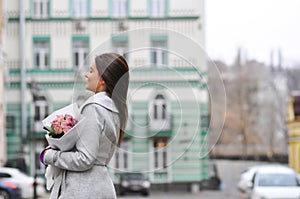 Beautiful young woman with flowers bouquet at city street. Spring portrait of pretty female