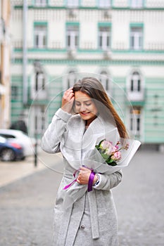 Beautiful young woman with flowers bouquet at city street. Spring portrait of pretty female