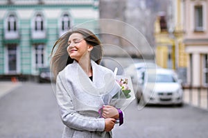 Beautiful young woman with flowers bouquet at city street. Spring portrait of pretty female