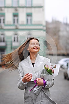 Beautiful young woman with flowers bouquet at city street. Spring portrait of pretty female