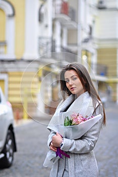 Beautiful young woman with flowers bouquet at city street. Spring portrait of pretty female