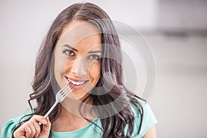 A beautiful young woman with a fork in her mouth is thinking with the temptation to eat