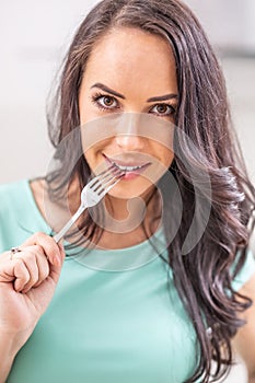 A beautiful young woman with a fork in her mouth is thinking with the temptation to eat