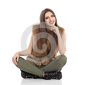 Beautiful Young Woman In Fur Waistcoat Is Sitting With Legs Crossed