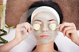 Beautiful young woman is getting facial clay mask at spa, lying