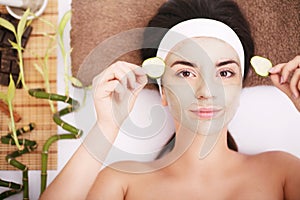 Beautiful young woman is getting facial clay mask at spa, lying