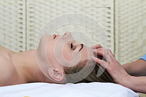 Beautiful young woman getting facial massage in the spa salon, close-up portrait, side view