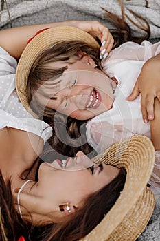 Beautiful young woman with girl in field with poppies, mother and daughter in white dresses and straw hats in evening at sunset,