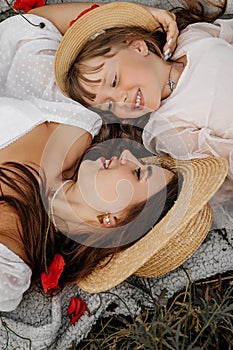 Beautiful young woman with girl in field with poppies, mother and daughter in white dresses and straw hats in evening at sunset,