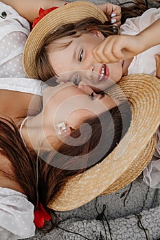 Beautiful young woman with girl in field with poppies, mother and daughter in white dresses and straw hats in evening at sunset,