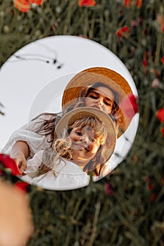 Beautiful young woman with girl in field with poppies, mother and daughter in white dresses and straw hats in evening at sunset,