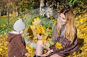 Beautiful young woman girl happy mother playing with her daughter smiling and holding a yellow maple leaves walking in autumn park