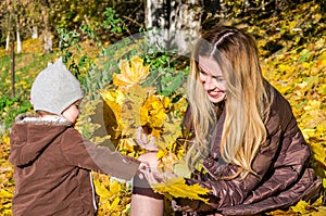 Beautiful young woman girl happy mother playing with her daughter smiling and holding a yellow maple leaves walking in autumn park