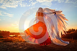 Beautiful young woman or girl in red dress and white wings on the sand on sunny day with blue sky. Angel model or dancer