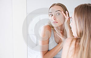 Beautiful young woman,girl is touching her face while looking at the mirror. Trouble on her skin