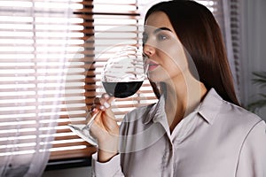 Beautiful young woman with glass of luxury red wine indoors